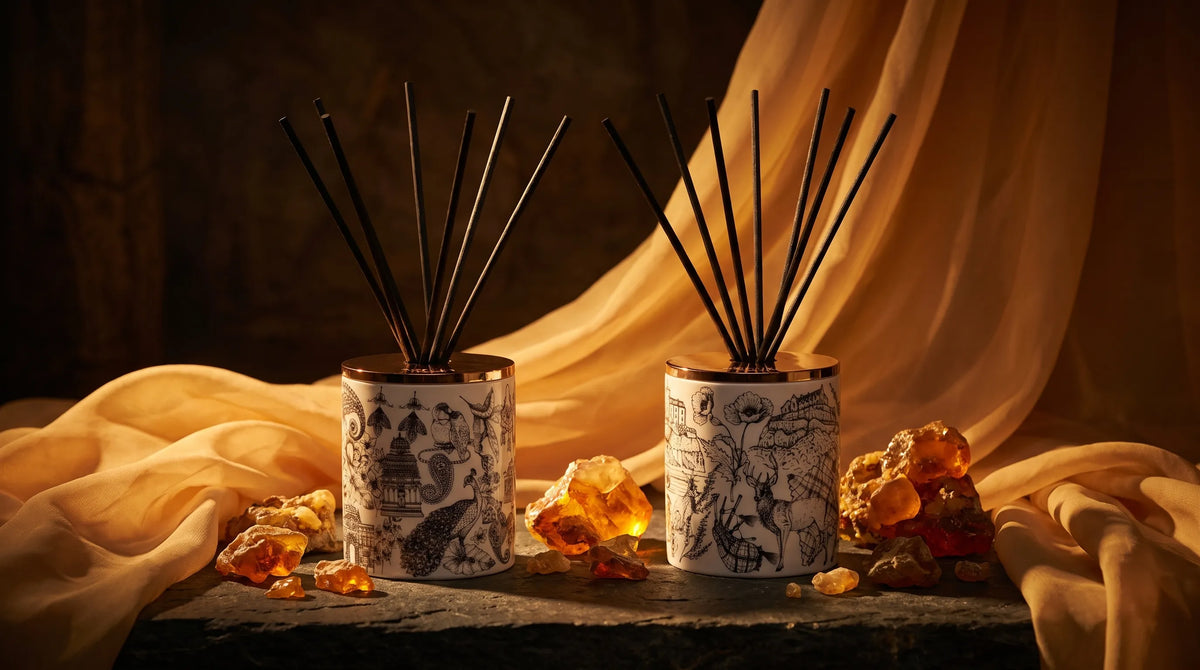 Two Told London reed diffusers with black reeds, Night Blooms and Highland Retreat, among pieces of amber resin and folds of ochre silk on dark slate.