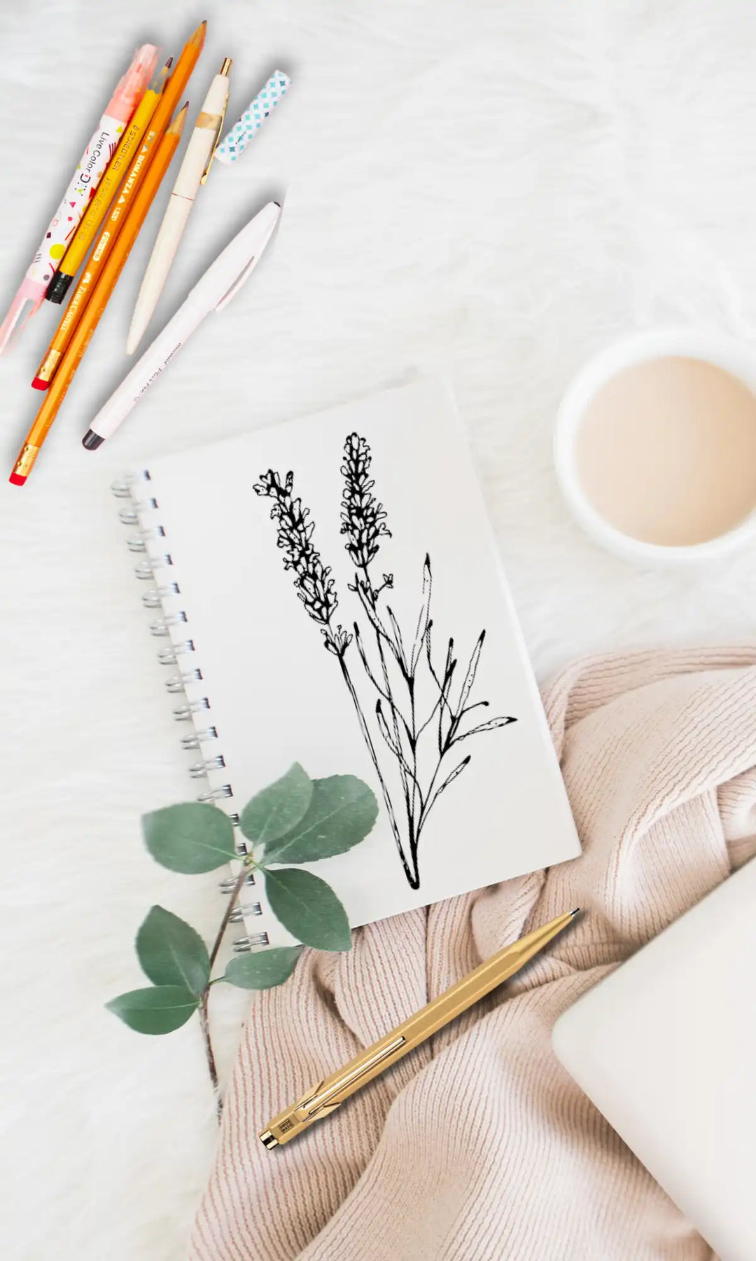 Black and white illustration of plant drawn on a notebook with a cup of tea and pile of pens and pencils