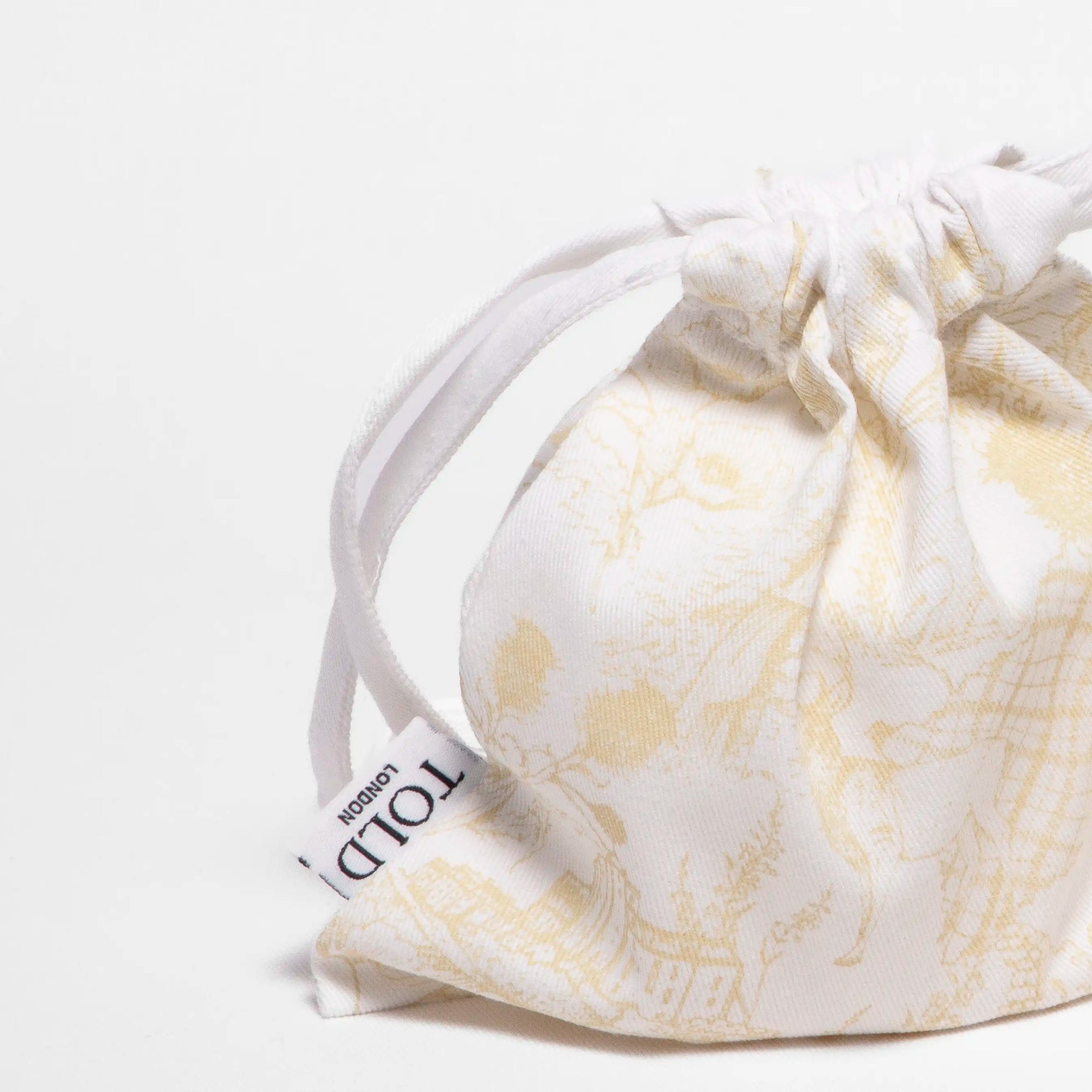 Close up of Told London' Highland Retreat candle refill bag, a cotton drawstring bag with golden linework illustrations.