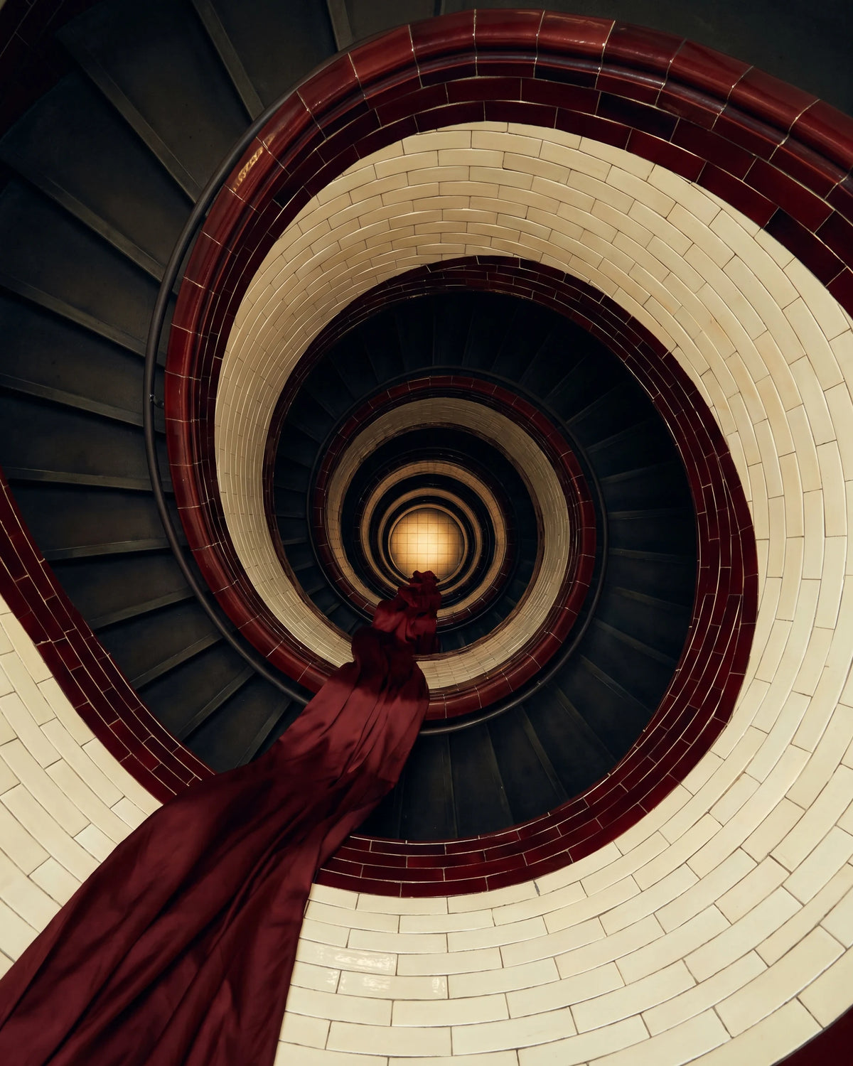 Looking down a cream-tiled spiral staircase, with oxblood silk falling through the centre.