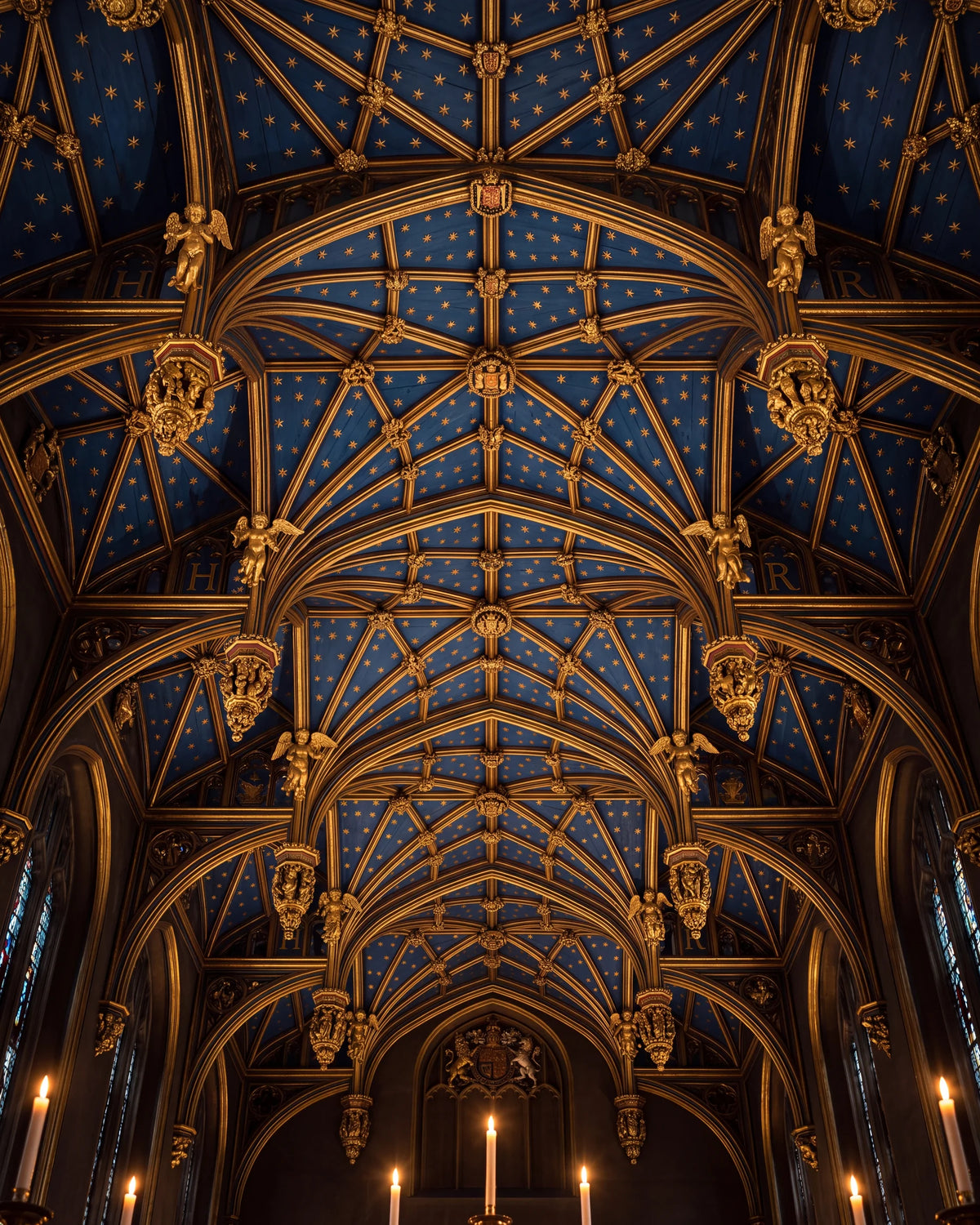 Looking up into the Chapel Royal ceiling at Hampton Court: deep blue vaulting with gilded stars and gold pendants, candles glowing below.