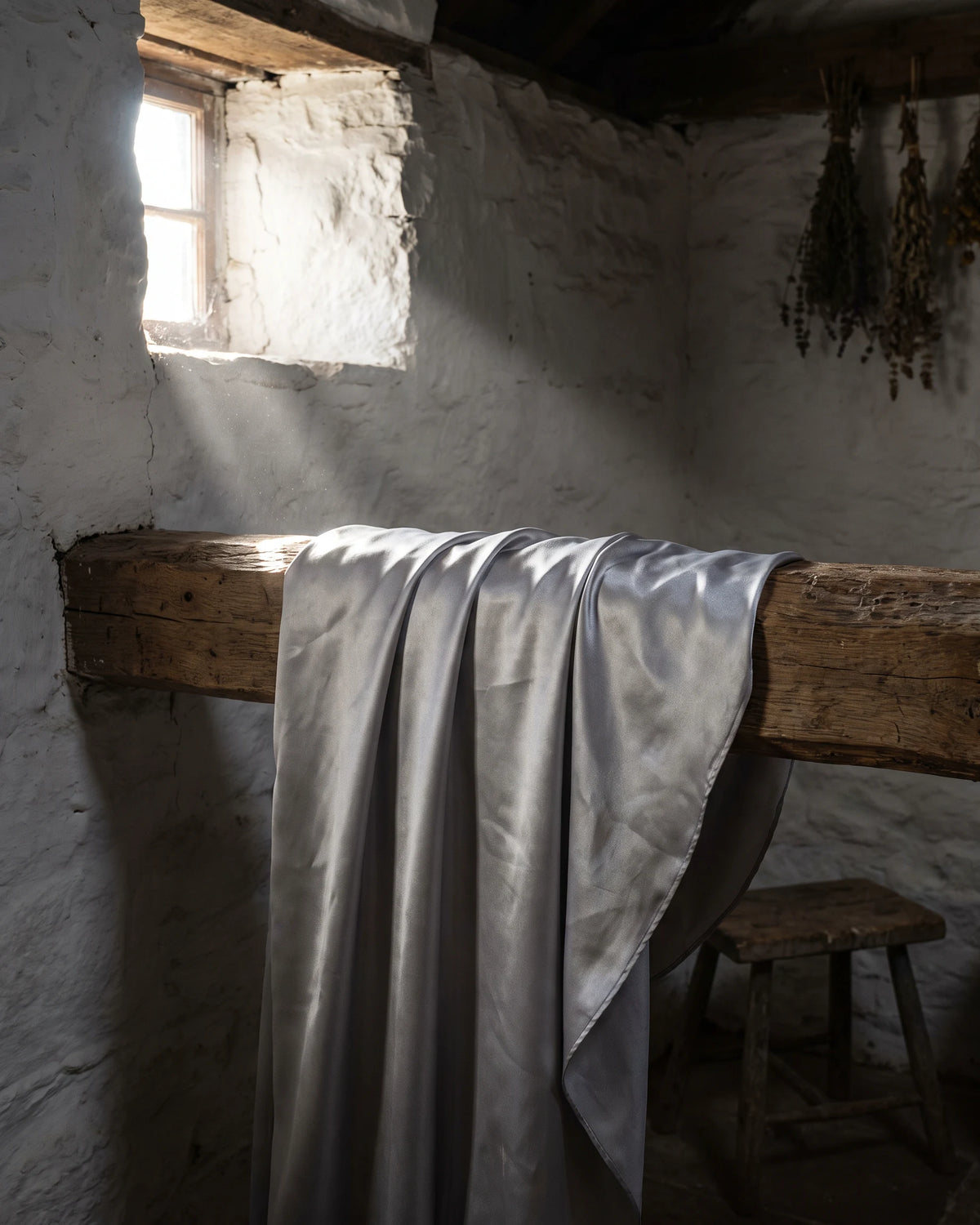 A silver cloak hung over a wooden beam inside a whitewashed croft, lit from a small window.
